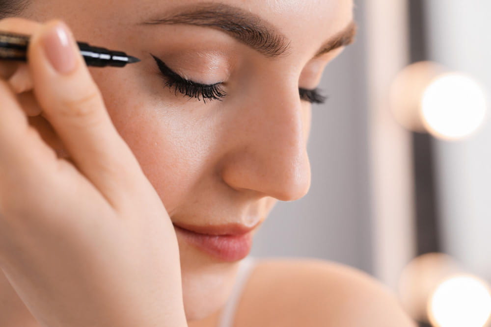 Kobieta wykonująca kreskę na oku za pomocą eyelinera